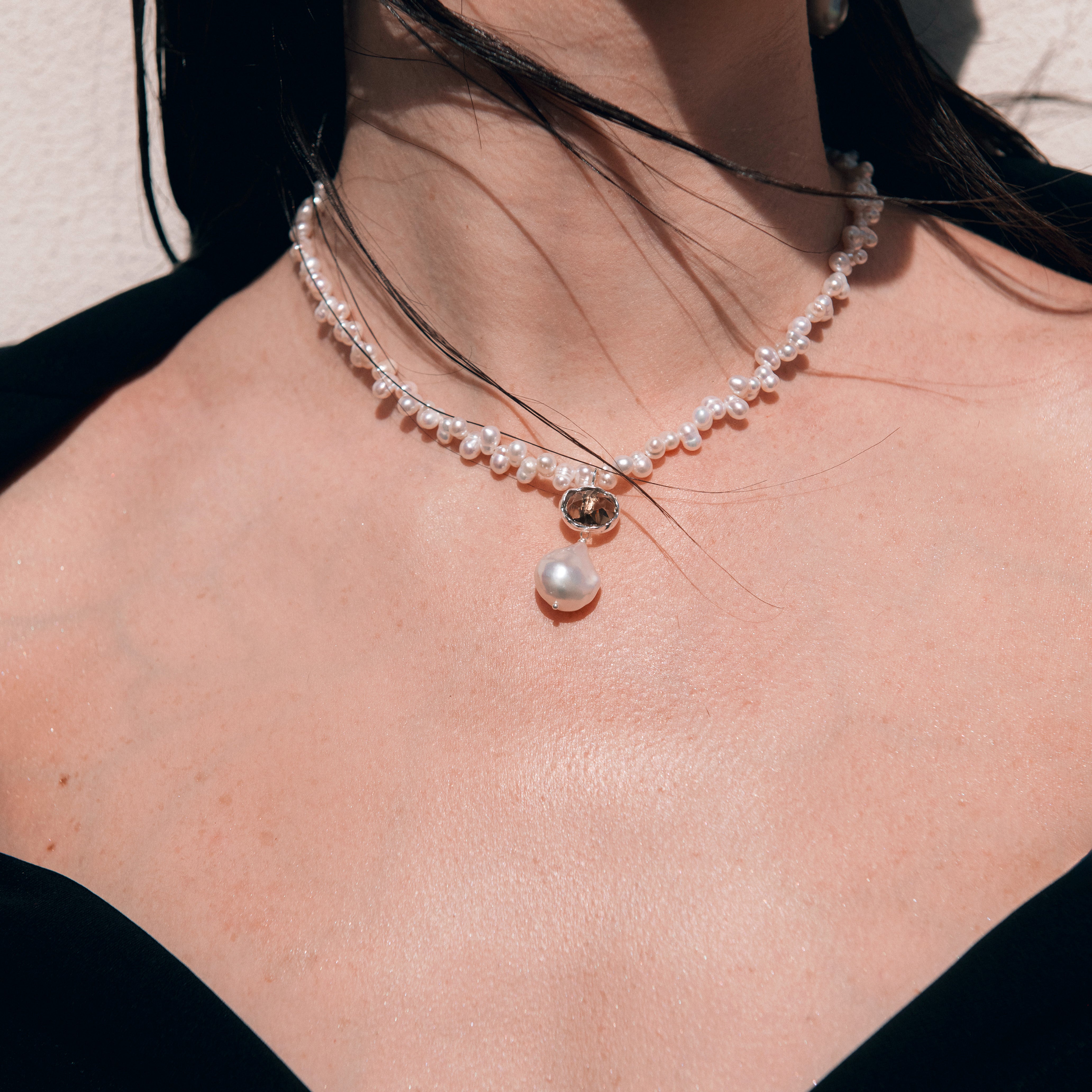 Pearl necklace with a pendant worn by a person against a neutral background